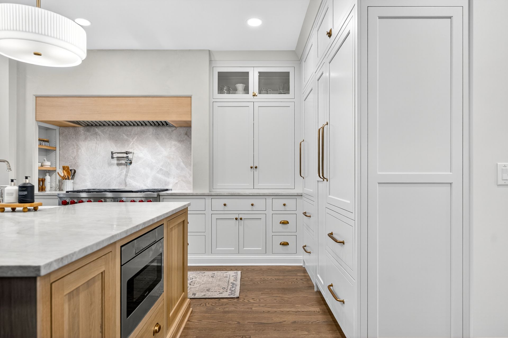 Bright, white kitchen with island and cabinetry. Wood and marble accents, gold hardware, and a range with hood.