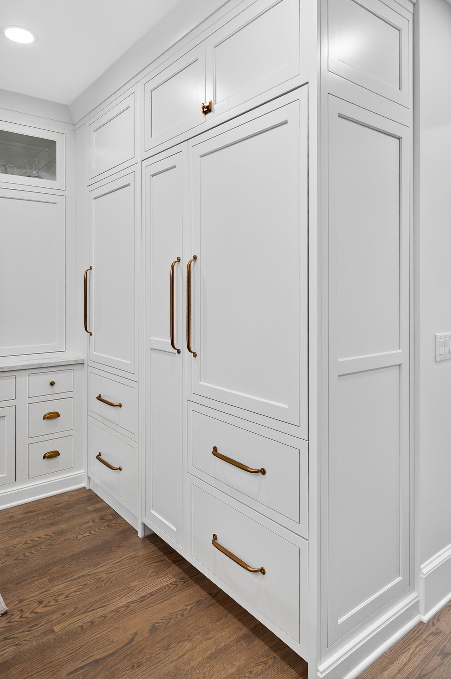 White cabinets with bronze handles in a room with hardwood flooring.