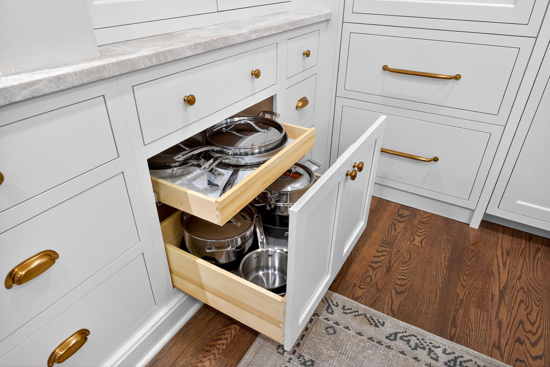 Open white kitchen cabinet with pull-out drawers holding pots and pans. Dark wood floor.