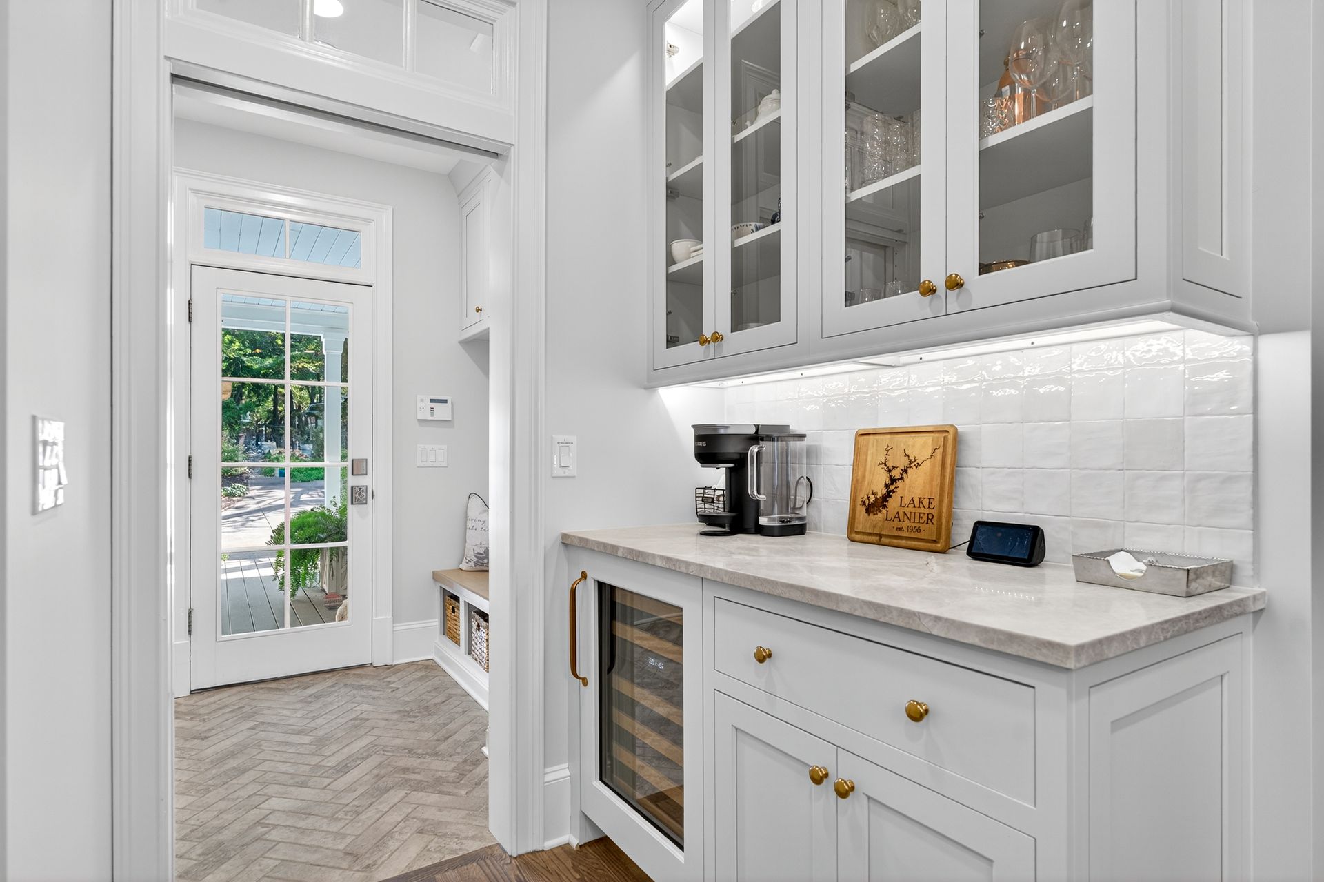 White kitchen pantry with glass-front cabinets, countertop, and a wine cooler. A doorway leads outside.