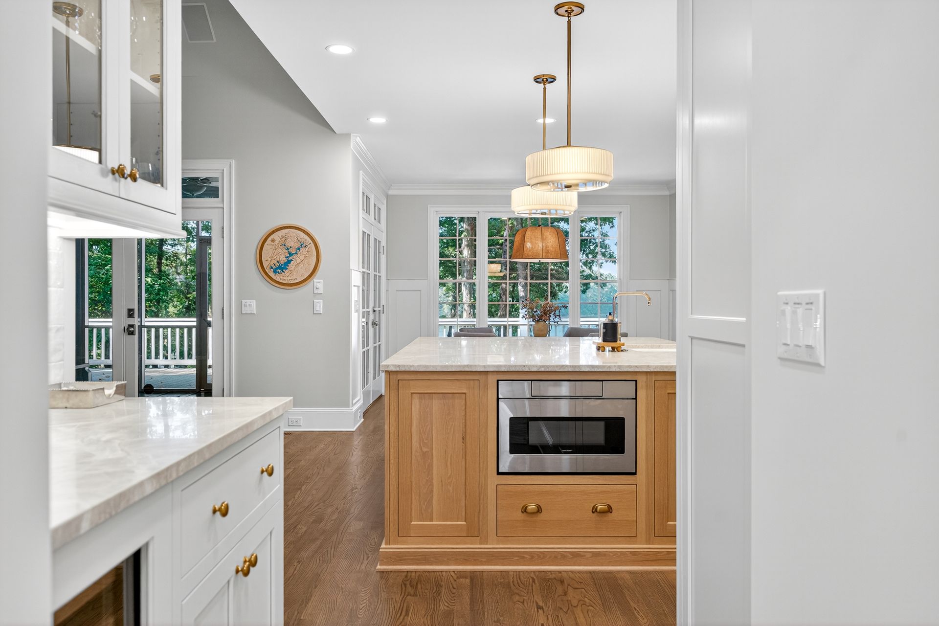 Kitchen with island, light wood cabinets, marble countertops, pendant lights, and a view of a patio.
