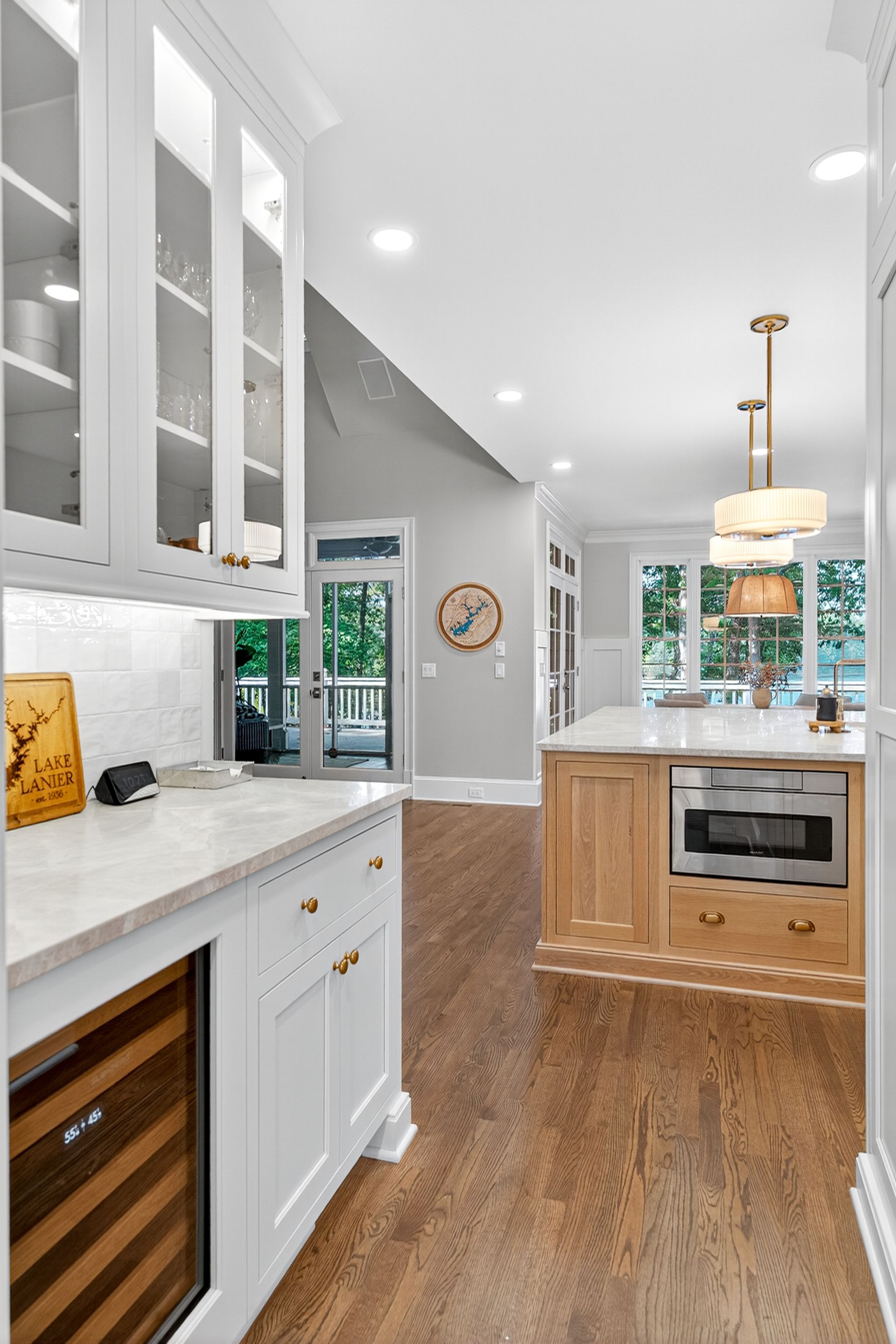 Kitchen with white cabinetry, light countertops, and wooden floors, leading to a light-filled space.