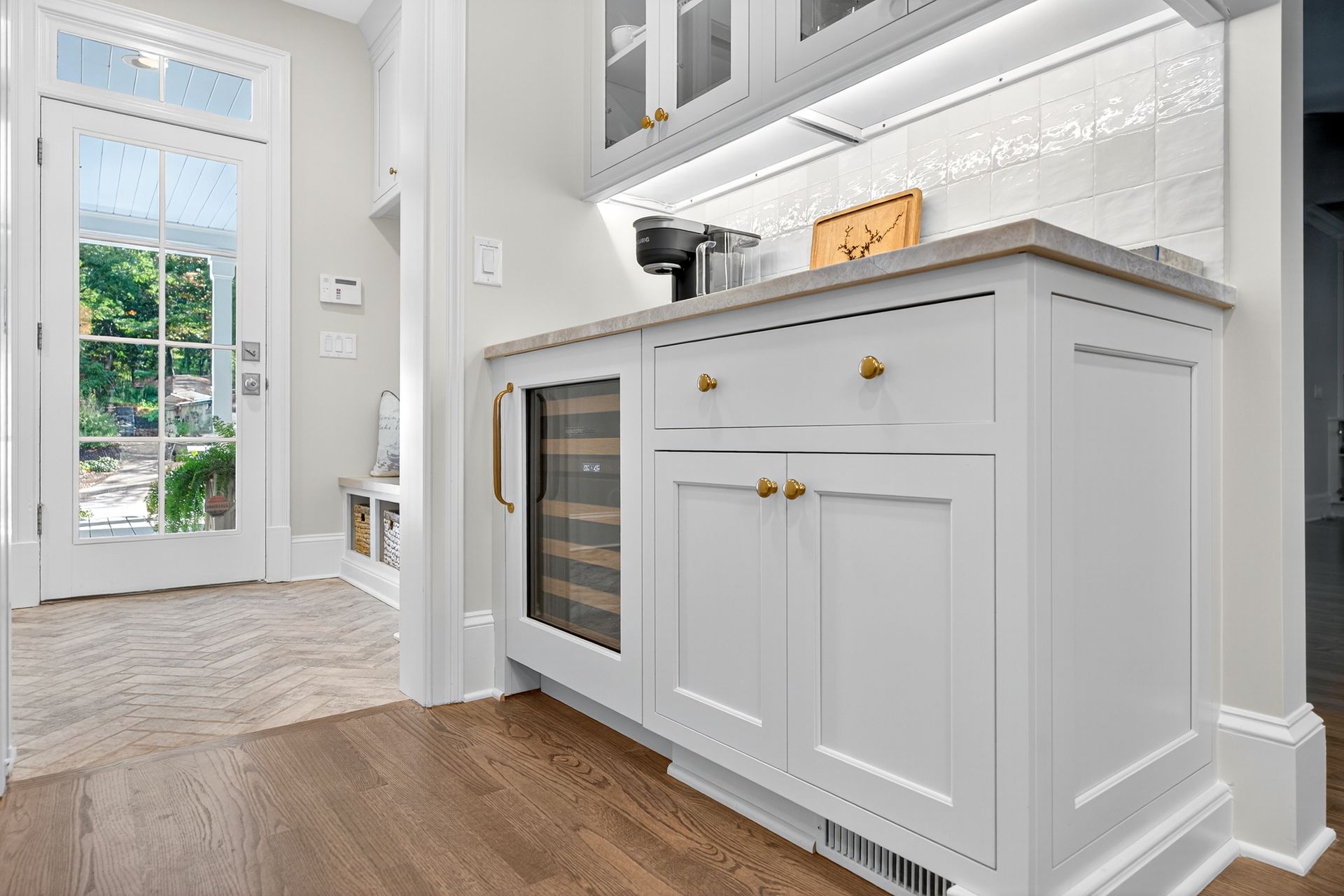 White cabinetry with wine fridge, countertop, and coffee maker in a light-filled entryway.