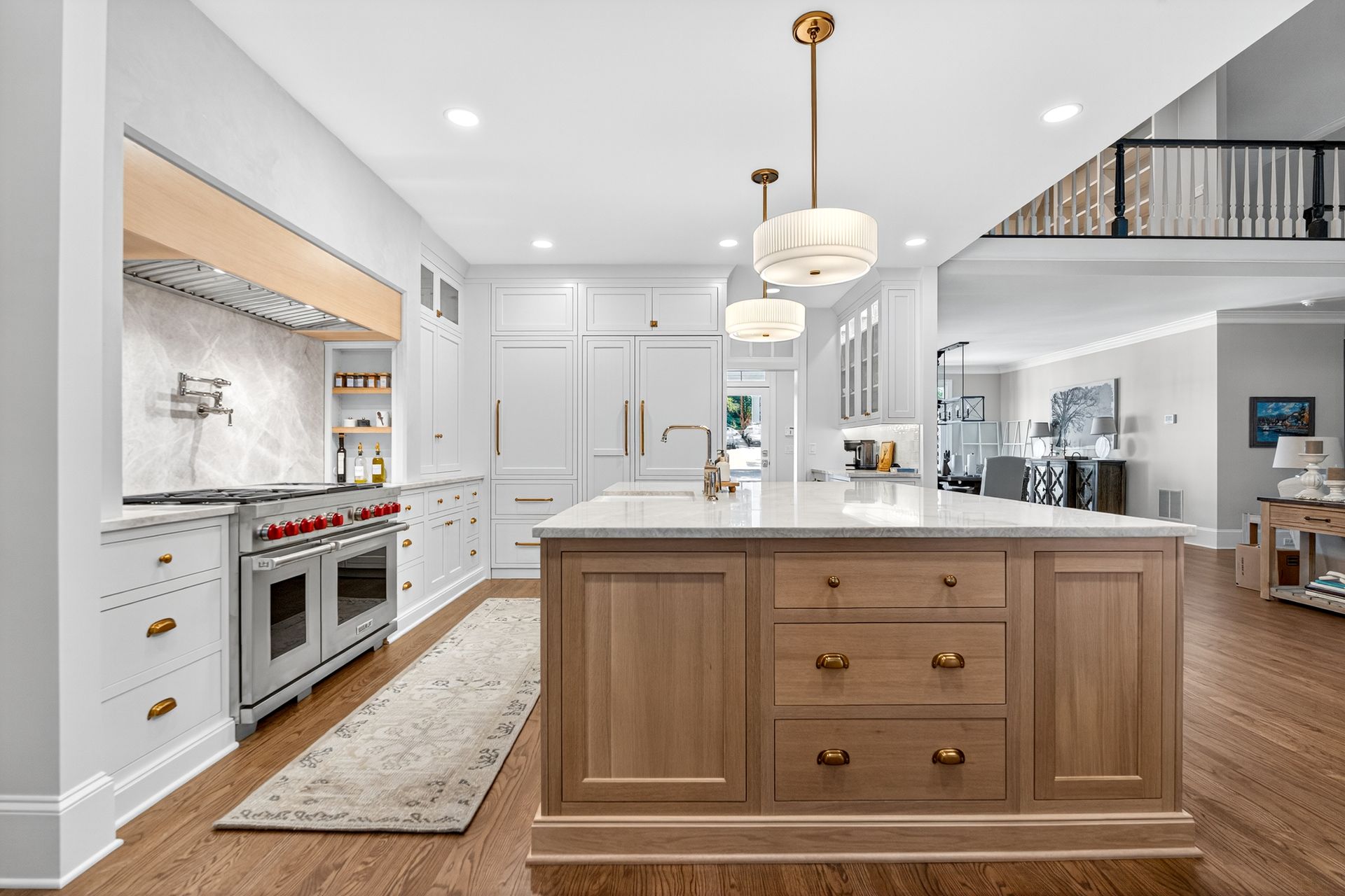 Bright white and wood kitchen with island, range, and two hanging lights. Hardwood floors.
