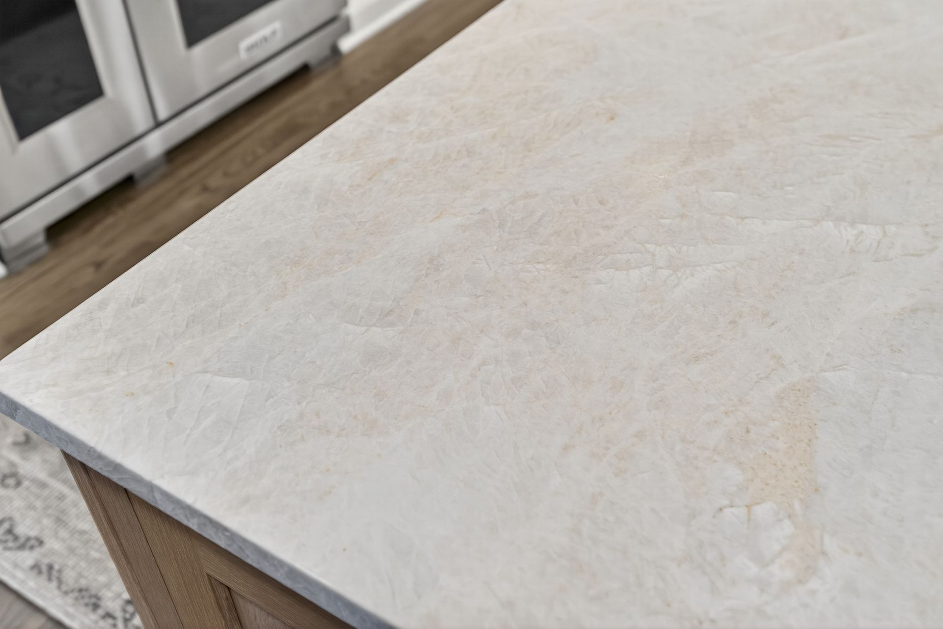 Close-up of a light-colored kitchen countertop with a marble-like pattern next to a stainless steel oven.