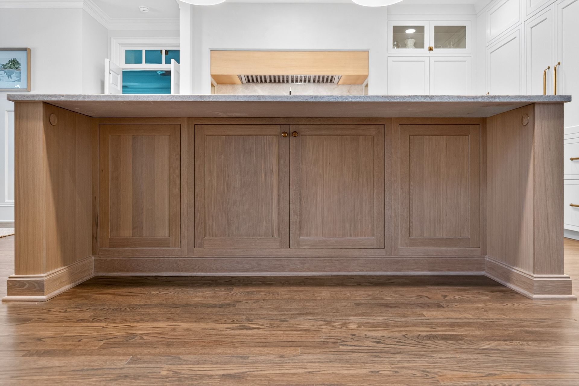 Wooden kitchen island with gray countertop, set in a light-filled kitchen with hardwood floors.