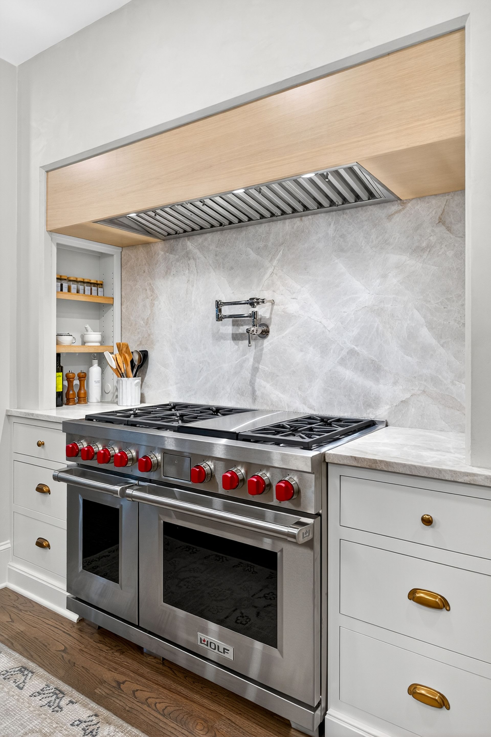 Stainless steel kitchen range with red knobs, white cabinets, and marble backsplash.