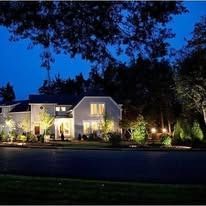 Well-lit suburban house at dusk with landscaped front yard and dark blue evening sky