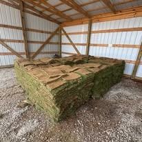 Stacked hay bales inside a wooden barn with a gravel floor