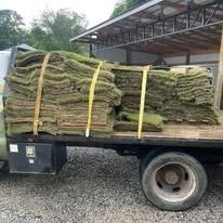 Flatbed truck loaded with stacked green sod rolls strapped with yellow bands
