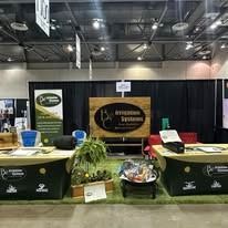 Trade show booth with black drapes, wood tables, green chairs, and a central sign reading “Epson System.”