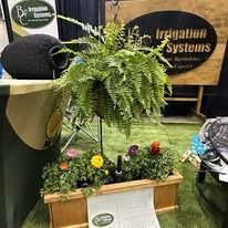 Indoor trade show display with hanging fern over flower bed, signage, and a banner for irrigation systems