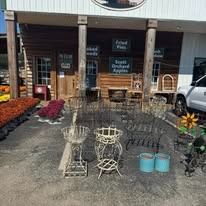 Outdoor storefront display with stacked metal chairs, small tables, and blue pots on a gravel patio