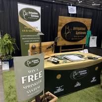 Booth display with wood sign, green banner, and “Win a free sprinkler system” sign at an expo.