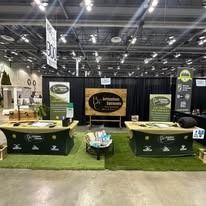 Trade show booth with green counters, black backdrop, and central logo display under bright expo hall lights