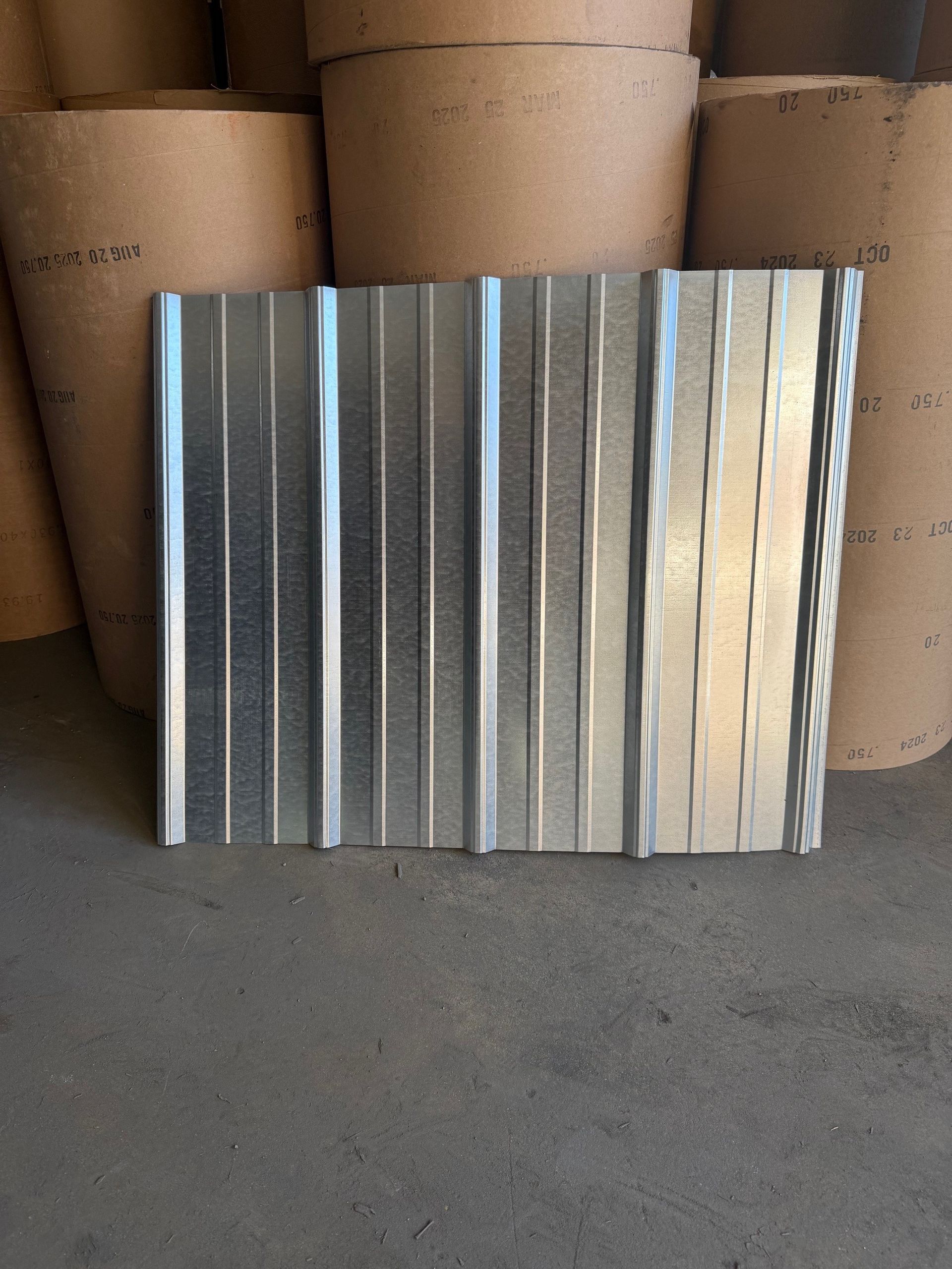A corrugated metal sheet standing in front of stacked rolls of industrial paper.