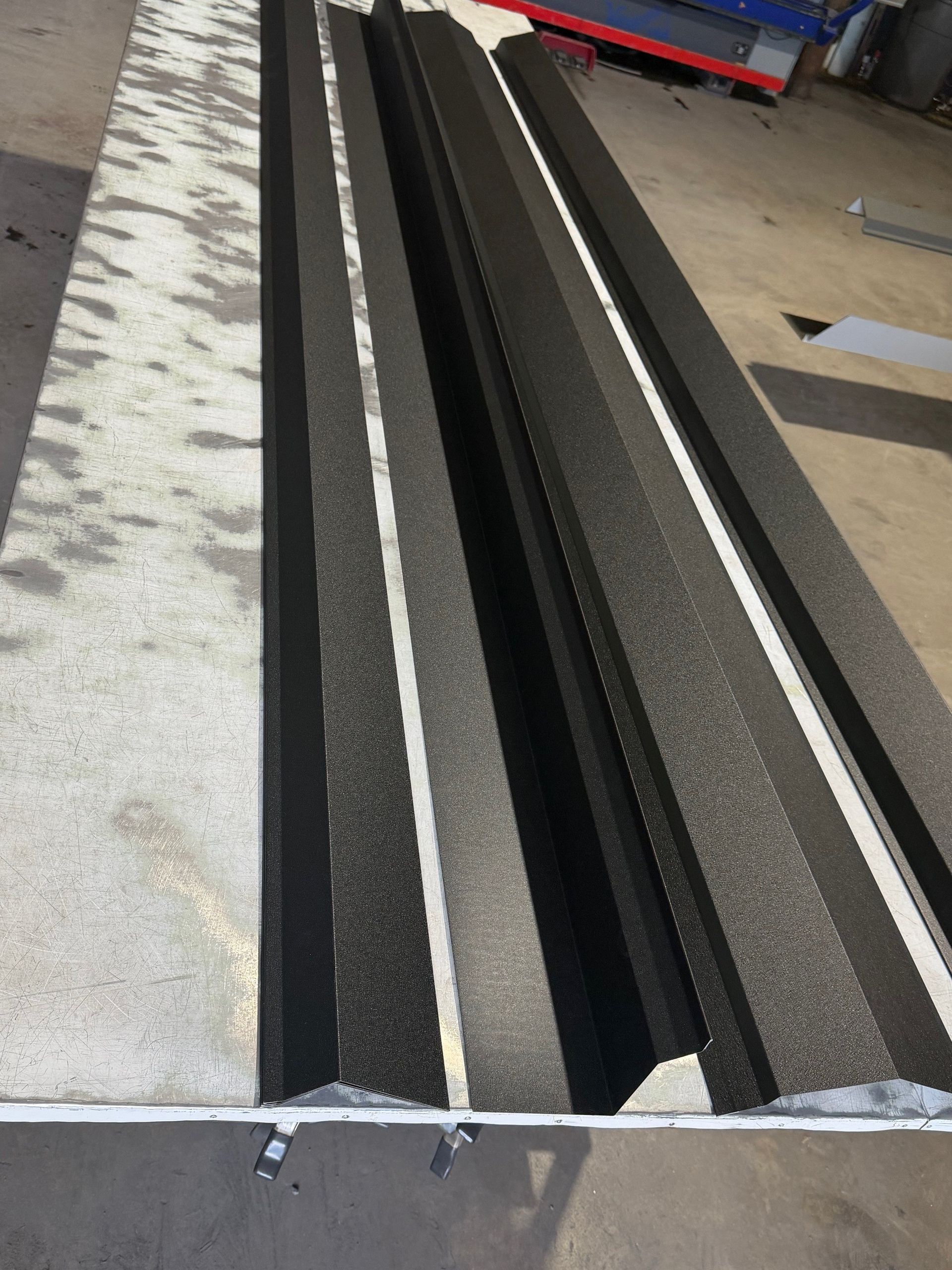 A long, rectangular panel featuring several black, textured, parallel ridge-like profiles on a workshop floor.