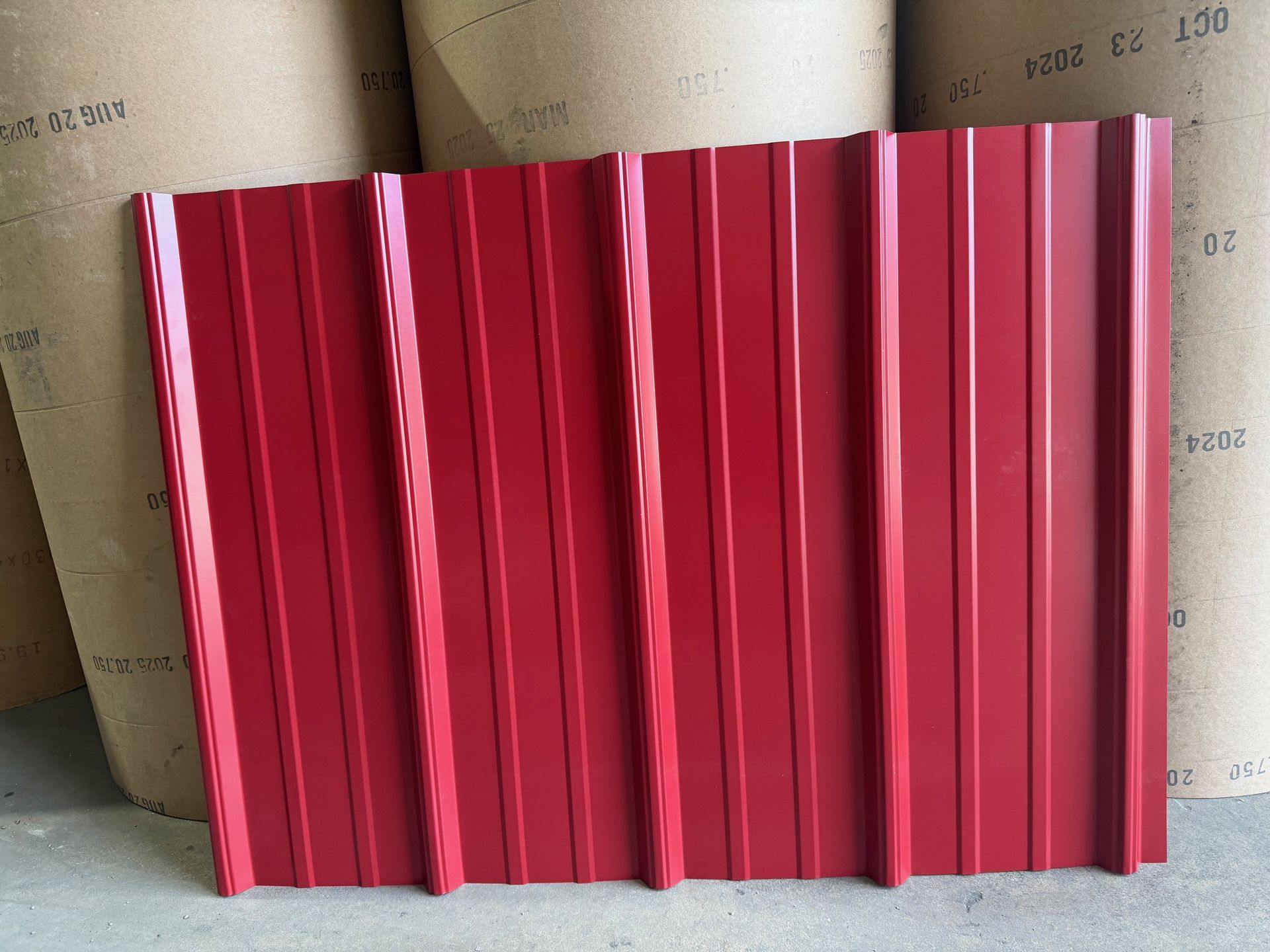 A piece of red corrugated metal roofing standing upright against large paper rolls.
