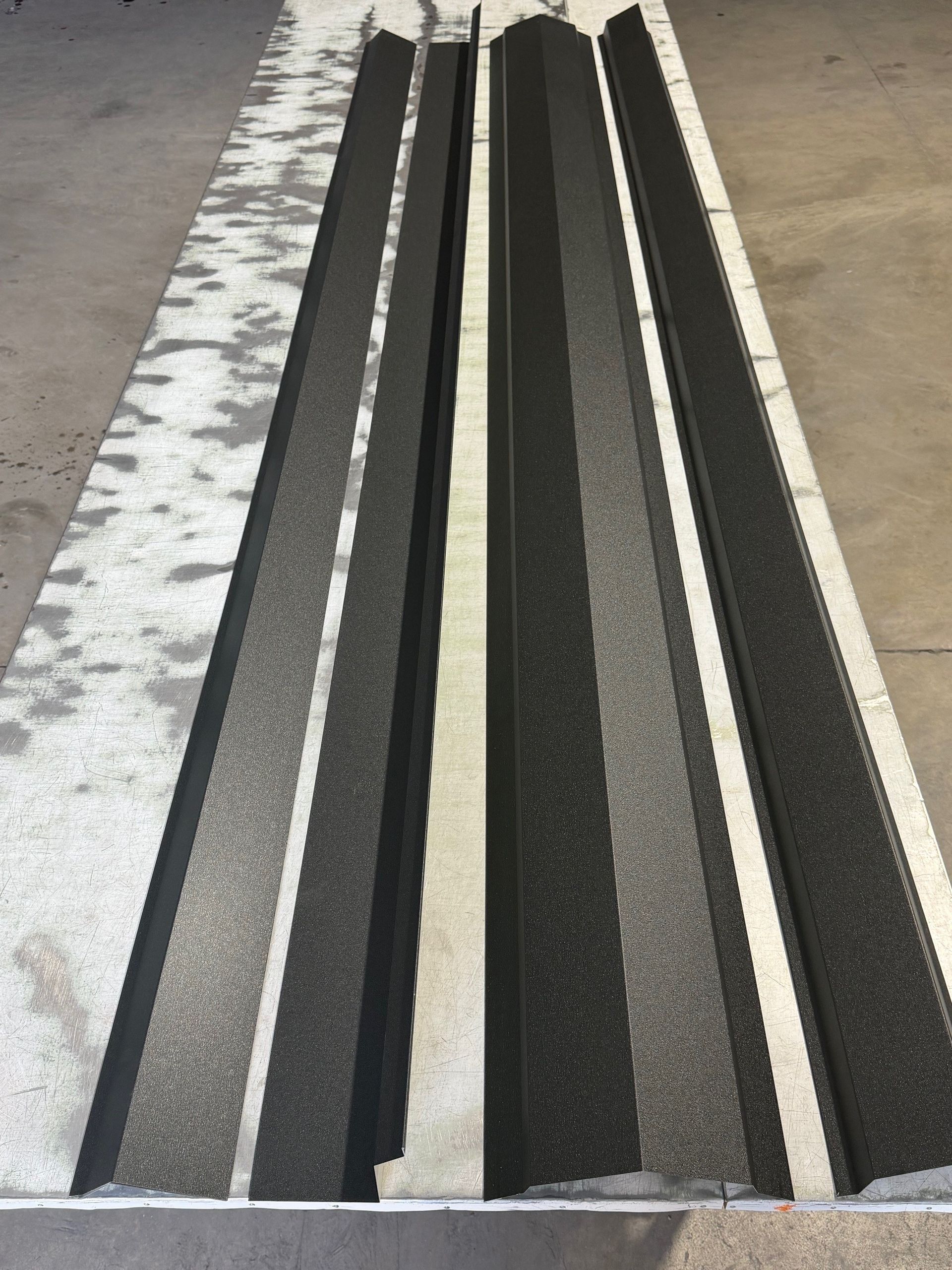 A top-down view of long, vertical strips of dark, textured material alternating with narrow, light-colored panels.