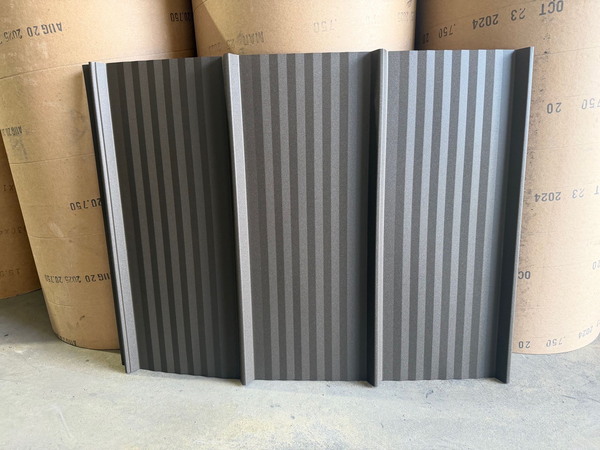 A dark brown, vertically corrugated metal panel standing upright in front of large paper rolls.