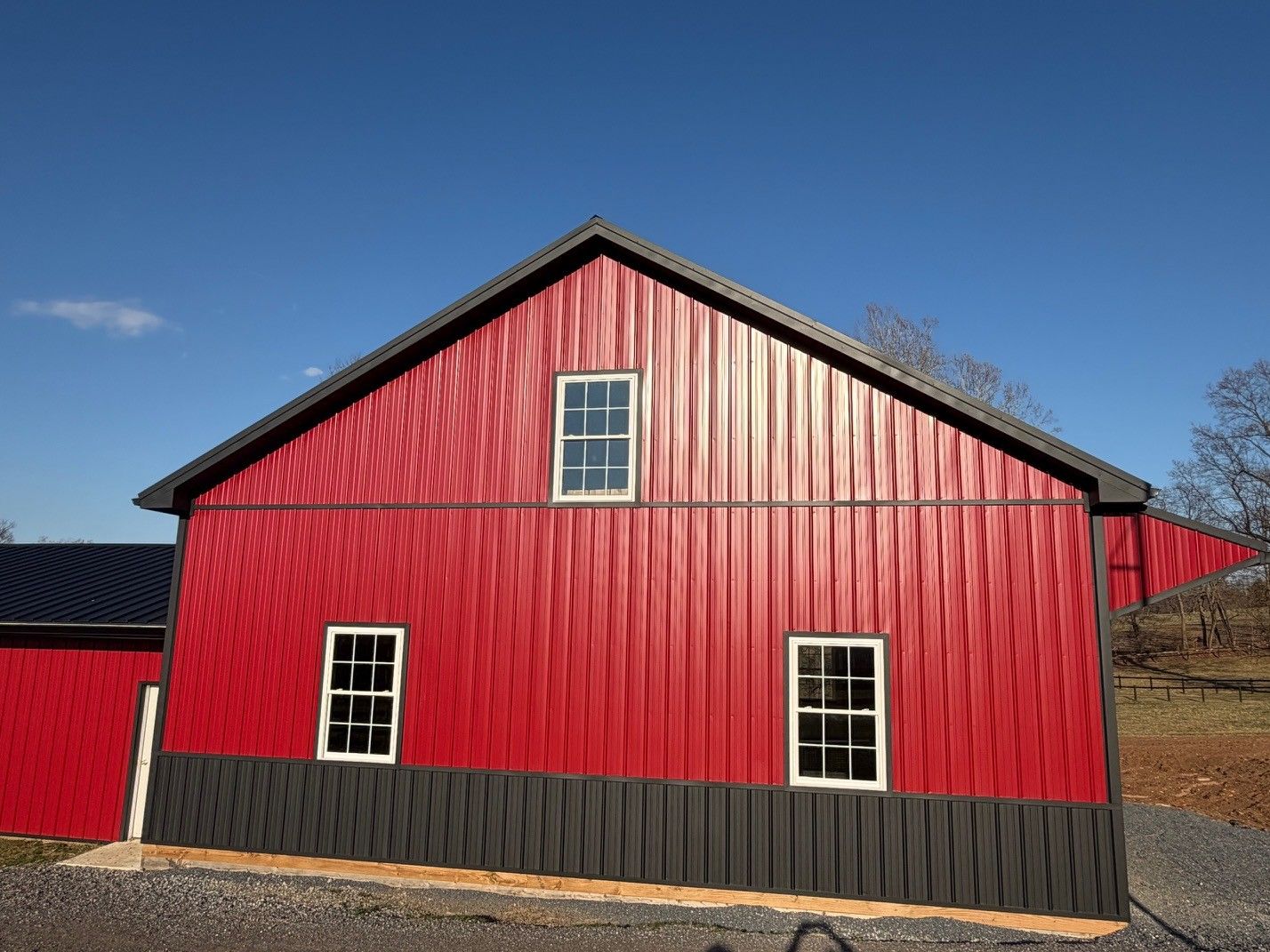 A red barn with a dark trim and gray base sits under a clear blue sky.