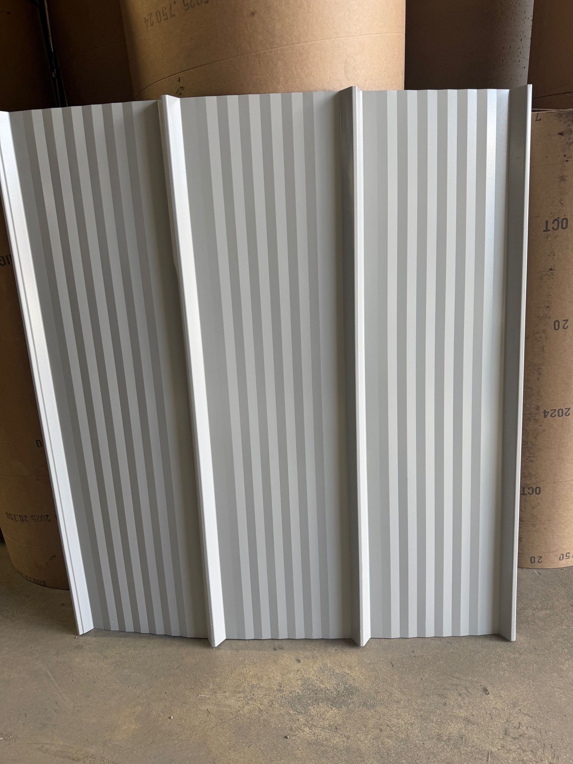 A light gray metal roofing panel featuring deep vertical ribs and a subtle textured, rippled surface pattern.