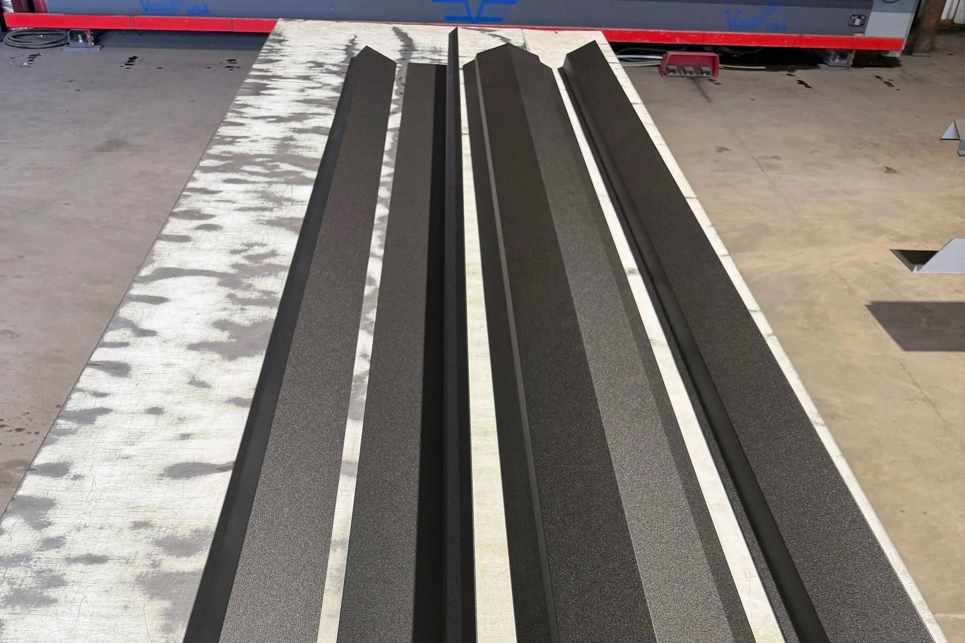 Two textured, dark grey molded panels lie parallel on a flat surface in a workshop.