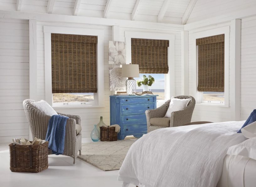 A bedroom with a bed , chairs , dresser and wicker blinds.