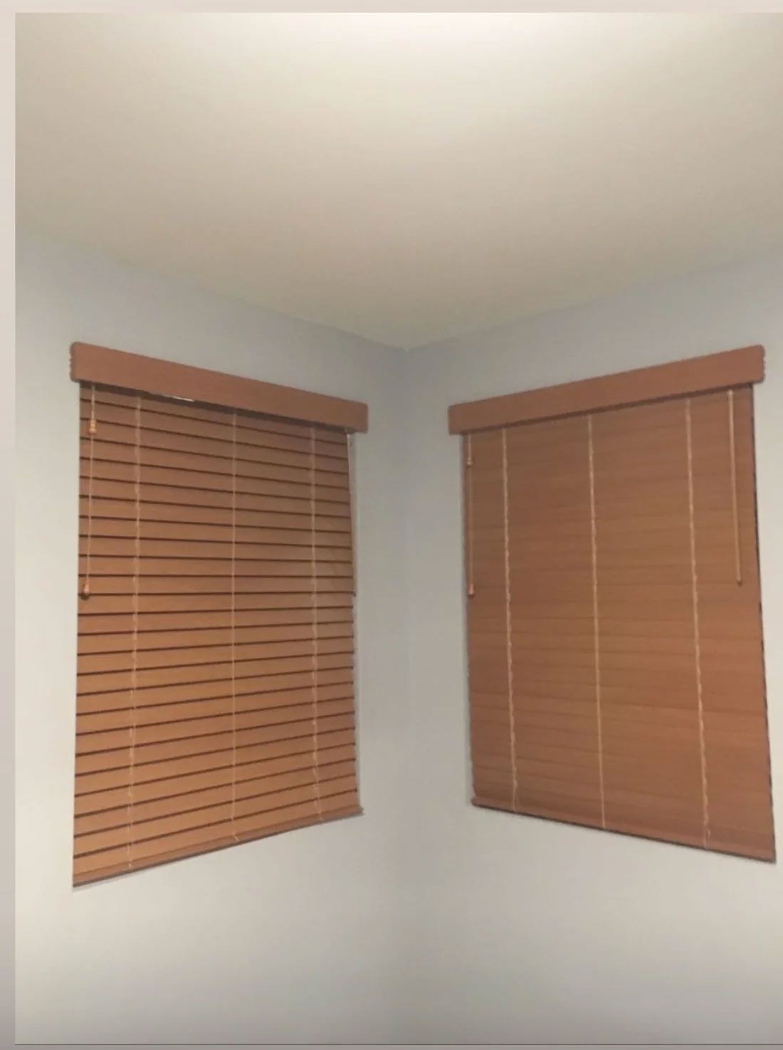 Corner of a room with two windows covered by tan wooden blinds.