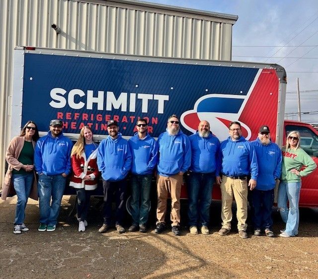 Group of people in blue shirts standing in front of a Schmitt Refrigeration truck, with a red pickup truck.