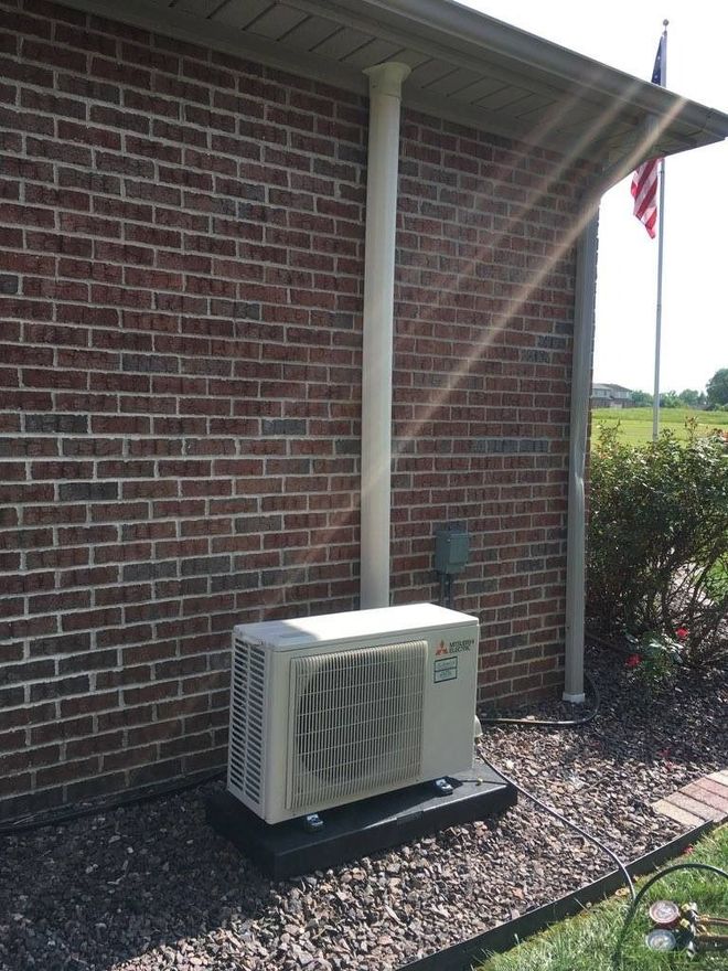 Brick wall with a white outdoor HVAC unit and vent pipe.