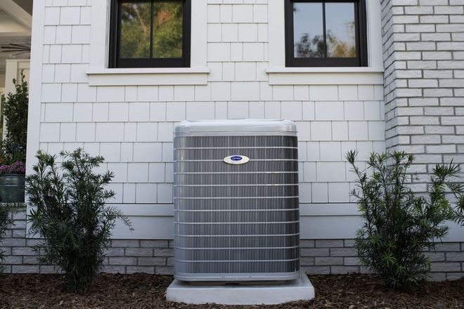 Air conditioner unit outside a white house with dark framed windows.