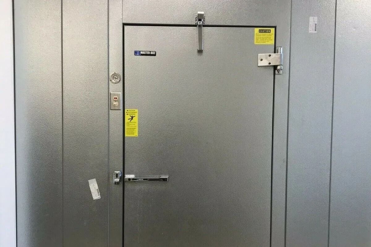 A metal walk-in cooler door with a handle, lock, and warning stickers.