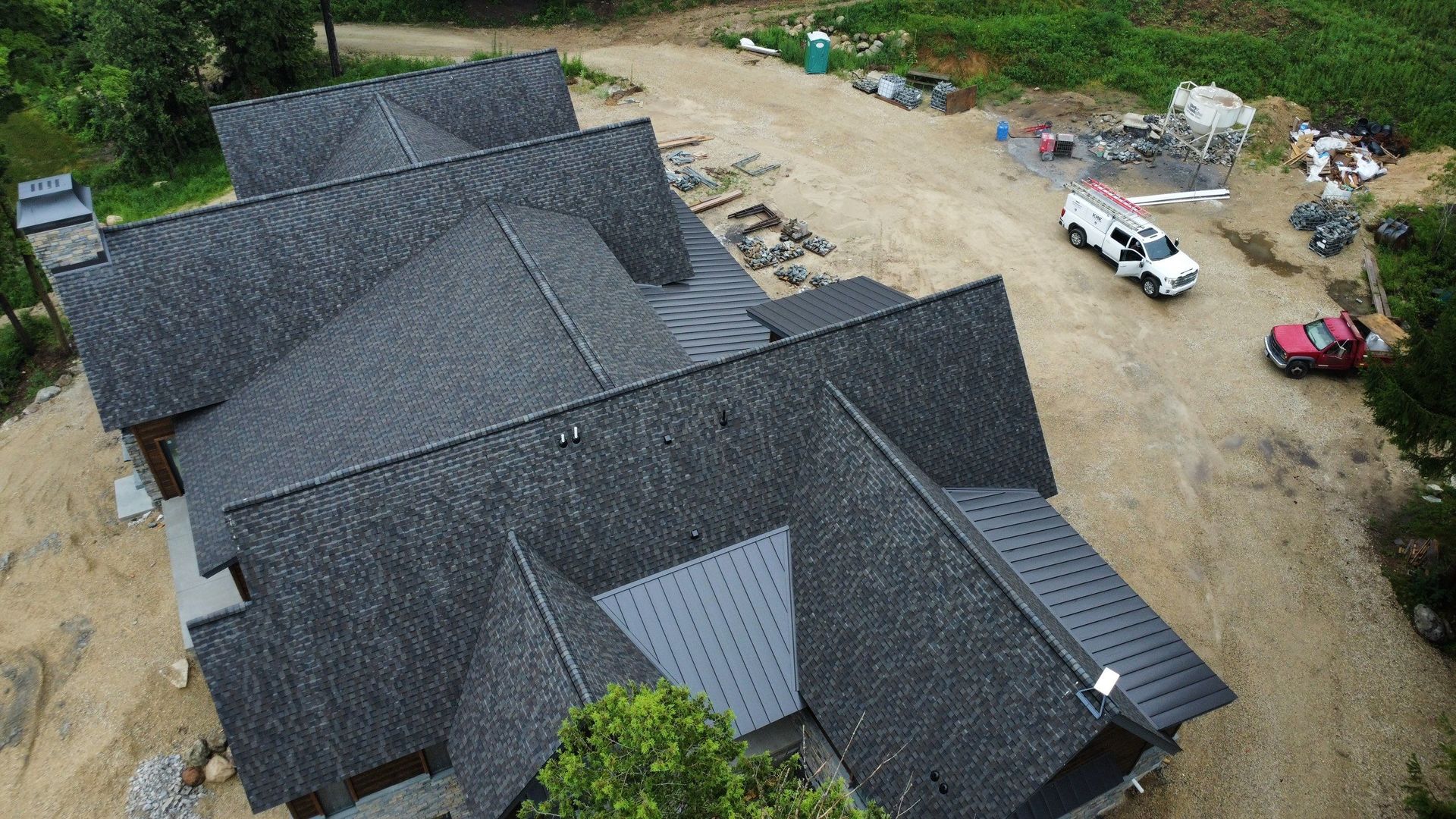 An aerial view of a large residential house under construction with a newly shingled roof, surrounded by dirt and a truck.
