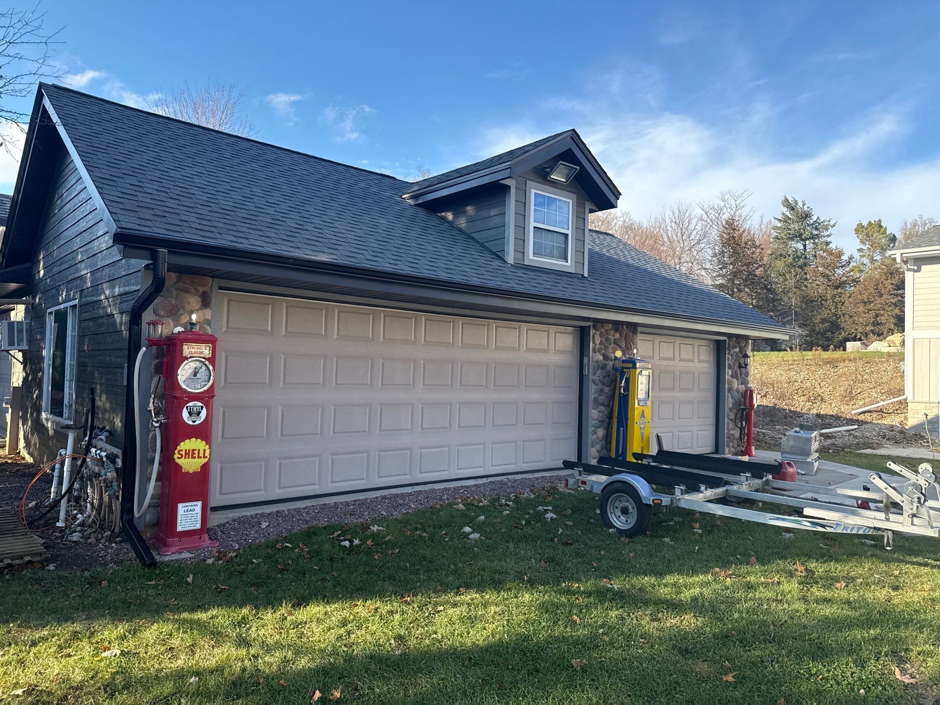 A detached garage with gray siding and a black metal roof, featuring a decorative red vintage gas pump in the front yard.