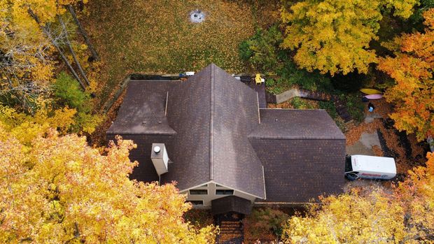 Aerial view of a house with a shingled roof surrounded by vibrant yellow and orange autumn trees.
