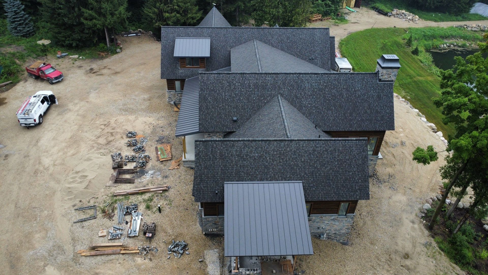 An aerial view of a house under construction with a dark shingled roof, surrounding dirt ground, and a work truck.