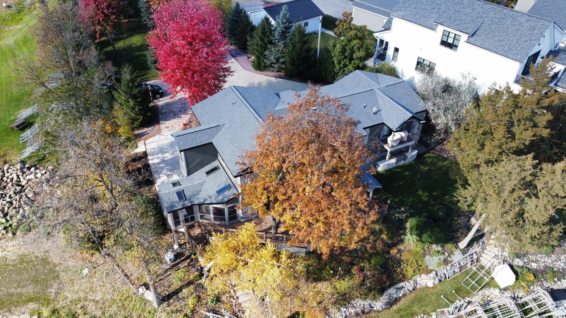 An aerial view of a large residential home surrounded by vibrant autumn trees in shades of red, yellow, and orange.