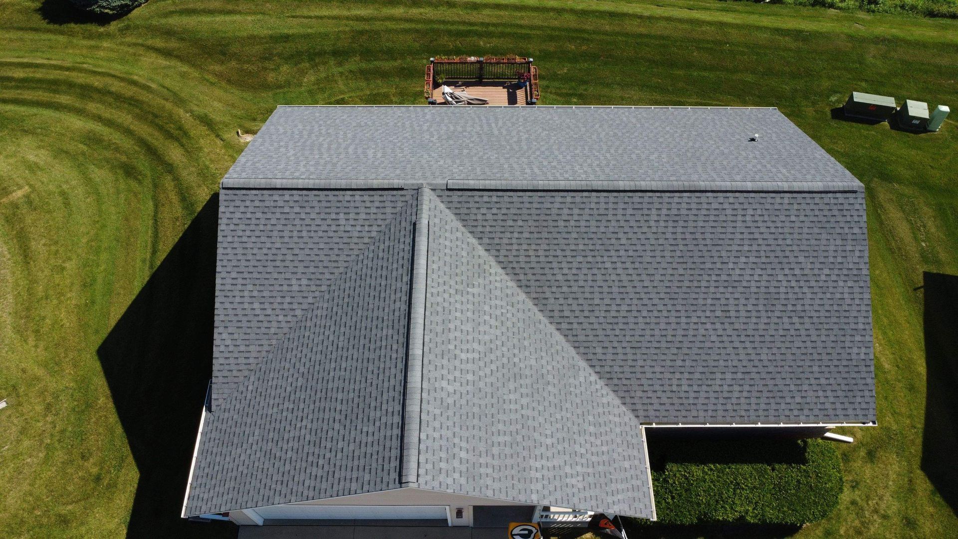 Aerial view of a gray asphalt shingle roof on a house, surrounded by a green grassy lawn.