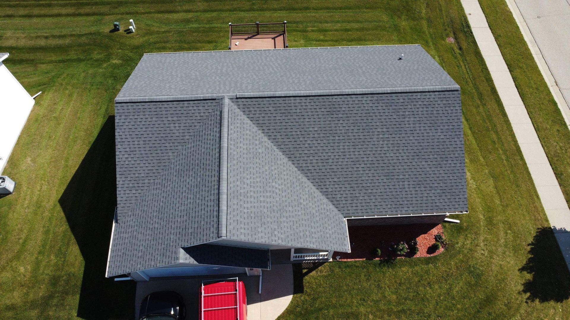 Aerial view of a residential grey shingled roof with a smaller attached section and a red dumpster in the driveway.