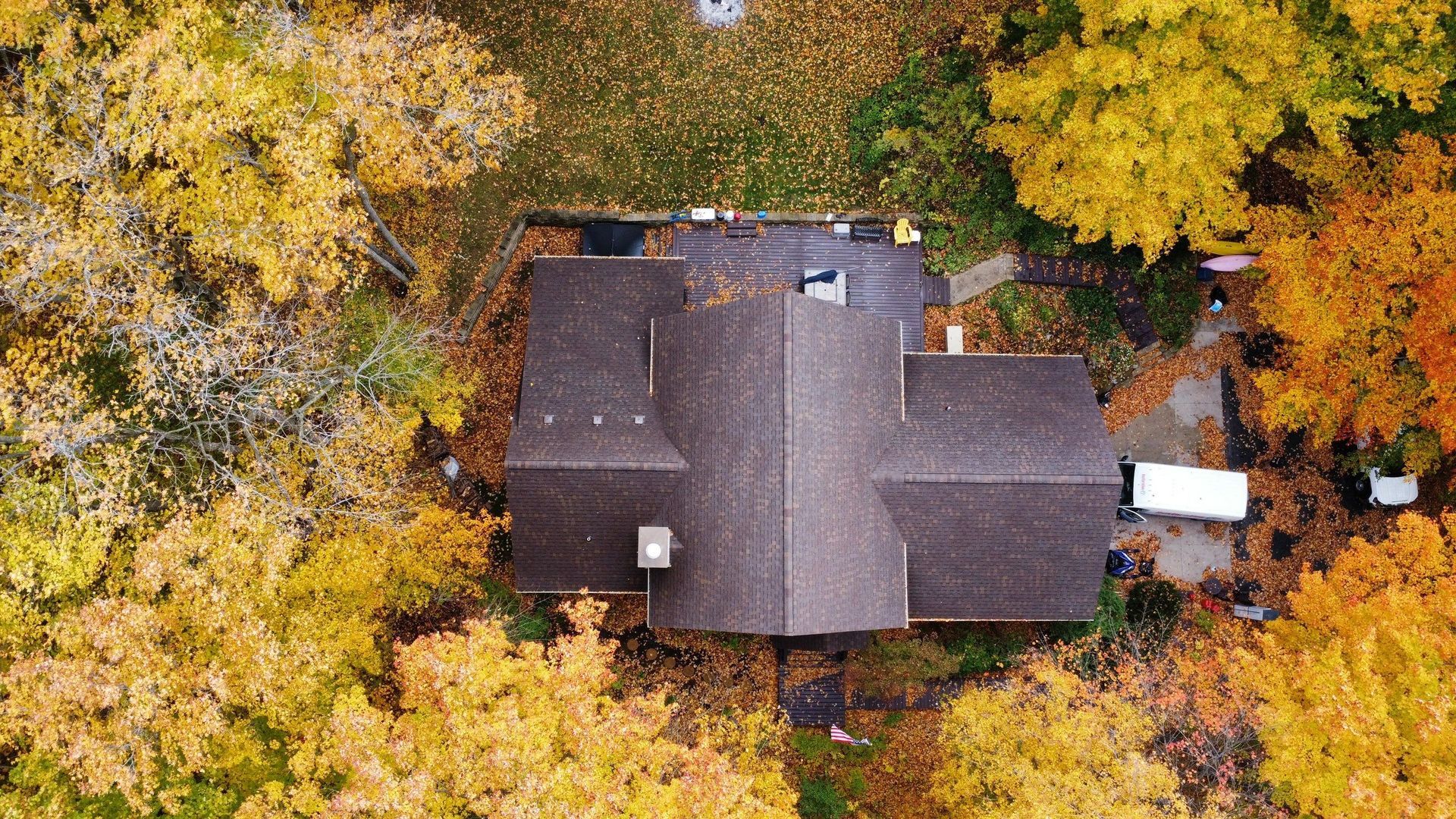 An aerial view of a house with a dark brown roof surrounded by dense, vibrant yellow and orange autumn trees.