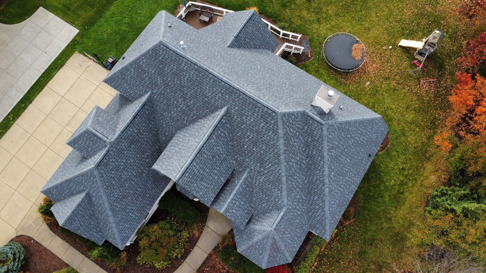 An aerial, top-down view of a dark grey shingled roof on a residential home with a driveway and backyard.