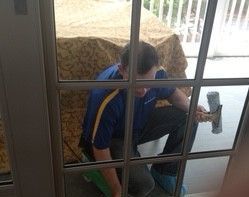 A man is cleaning a sliding glass door with a squeegee.