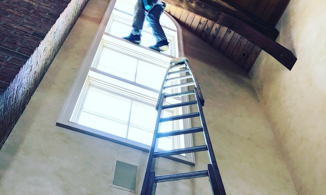 A man is standing on a ladder in front of a window.