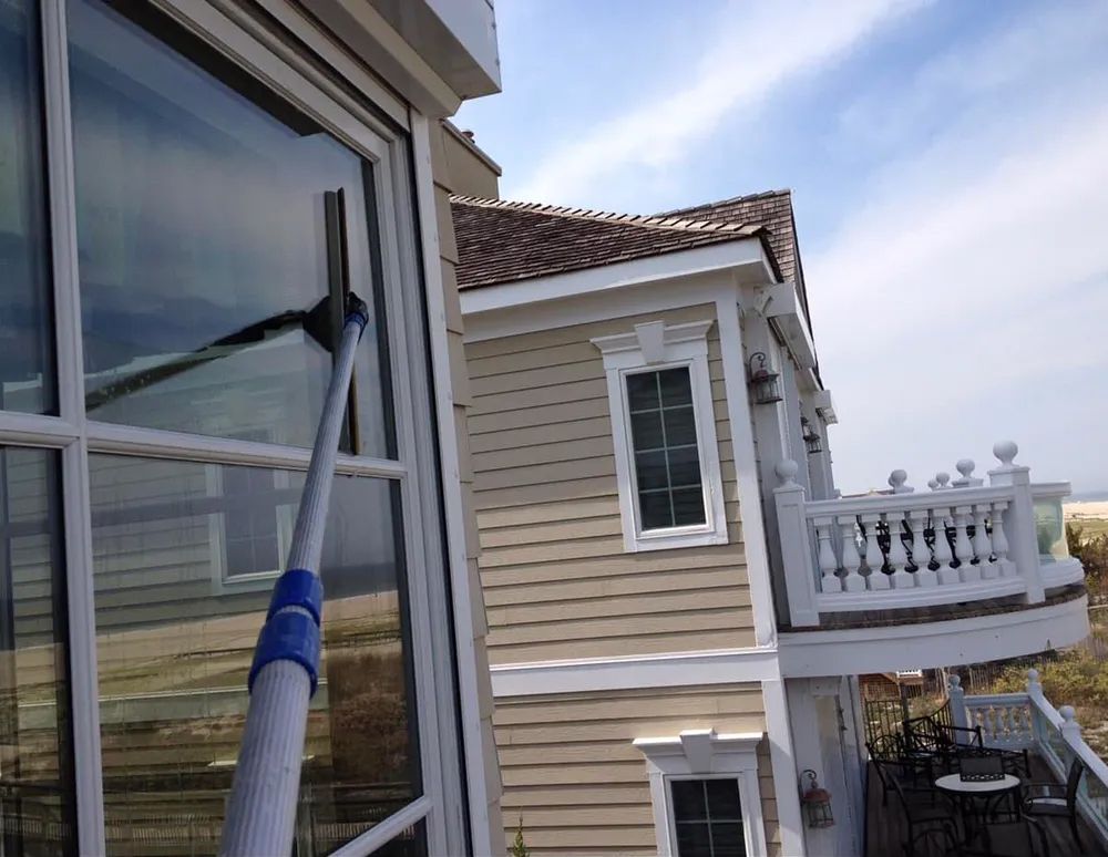 A person is cleaning a window with a mop in front of a house.
