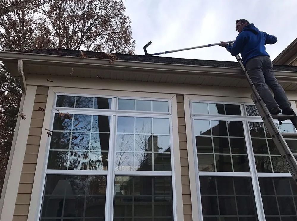 A man on a ladder is cleaning the roof of a house