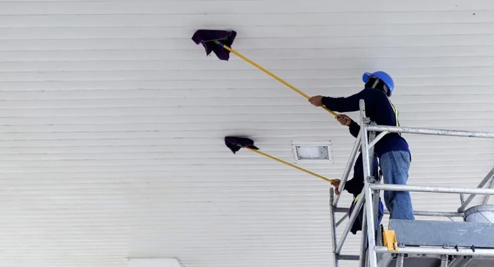A man is standing on a scaffolding cleaning the ceiling with a mop.