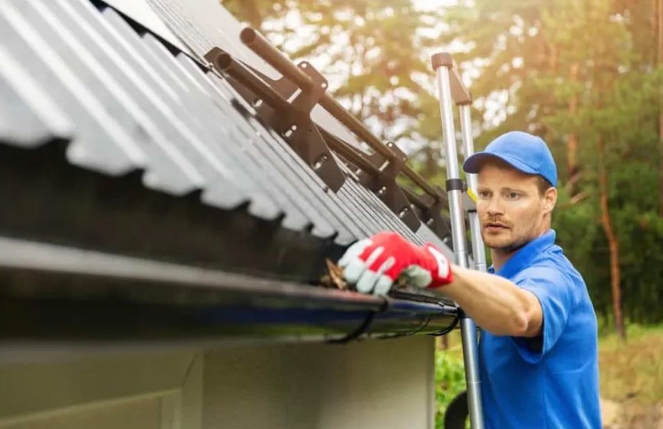 A man is cleaning a gutter on the roof of a house.