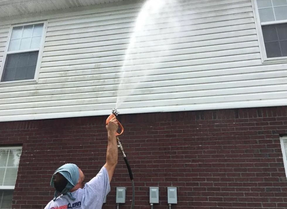 A man is cleaning the side of a house with a pressure washer.