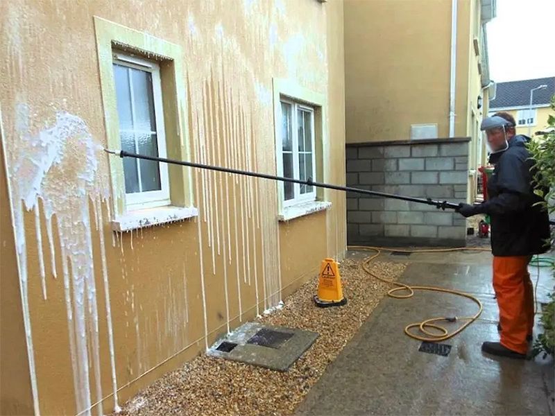 A man is cleaning the side of a building with a high pressure washer.